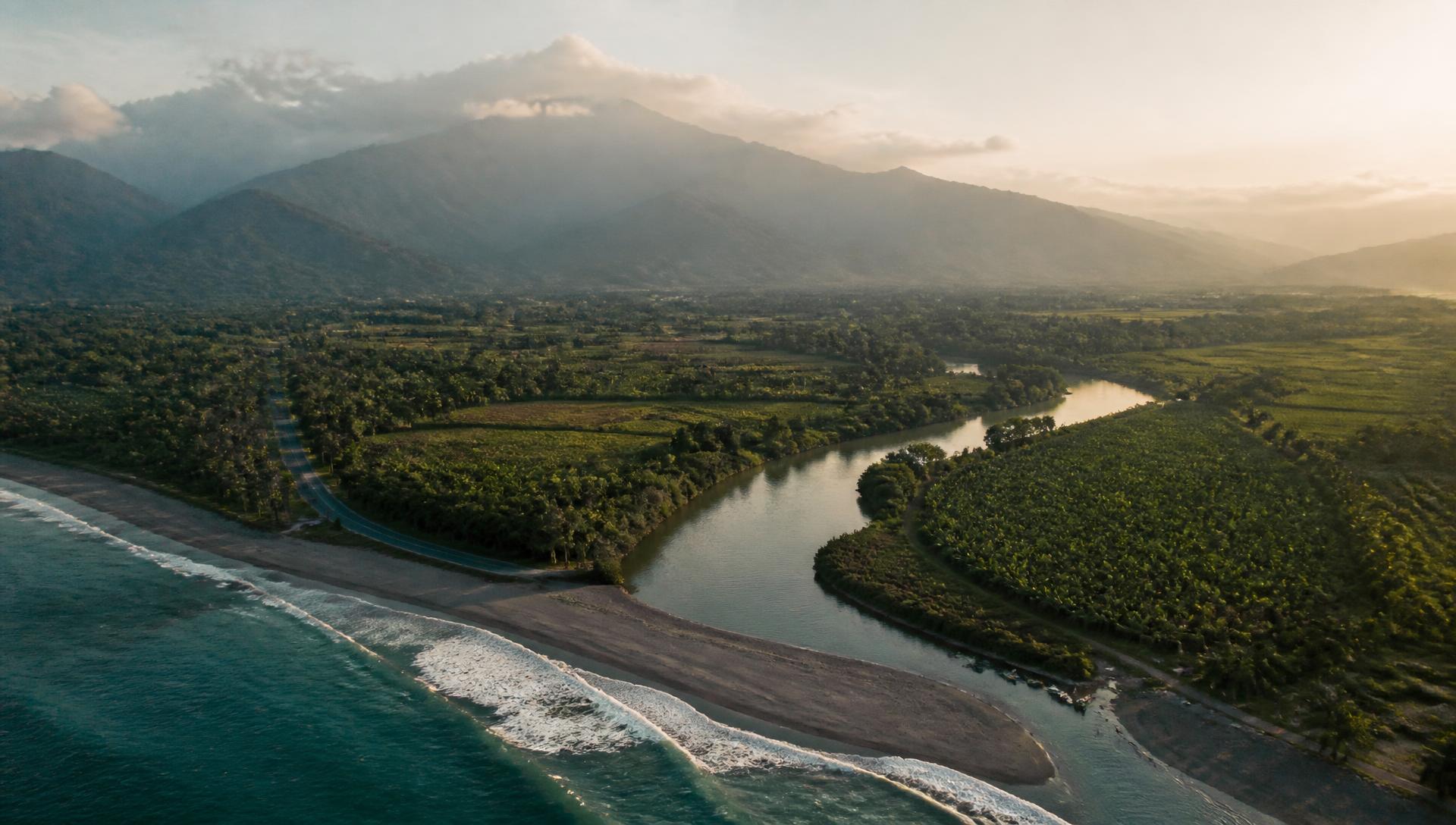 Vista aérea de un río que llega al Caribe, con cultivos y la vía costera bajo la Sierra Nevada